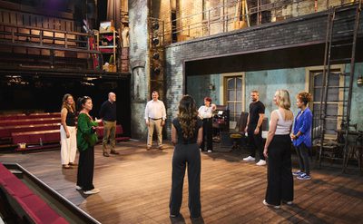 A group of people stand in a circle on a theatre stage