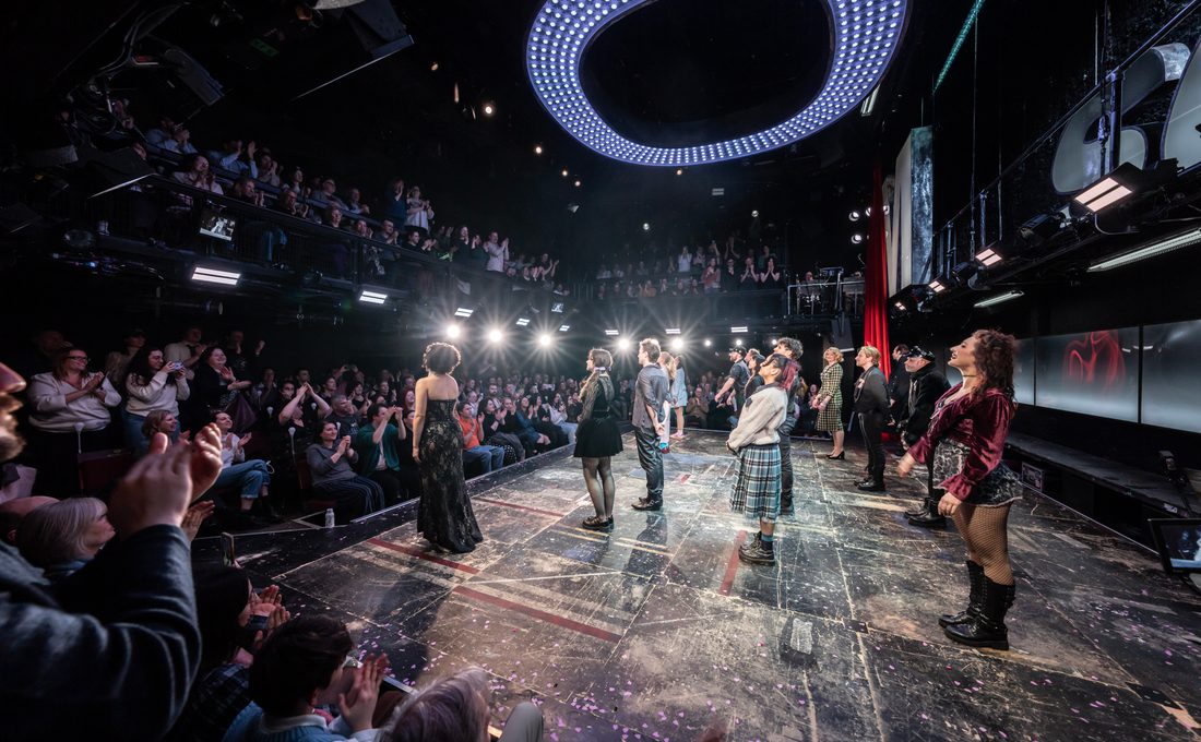 Actors stand on stage taking a bow as the audience are on their feet clapping enthusiastically