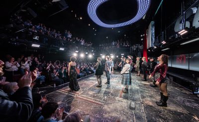 Actors stand on stage taking a bow as the audience are on their feet clapping enthusiastically