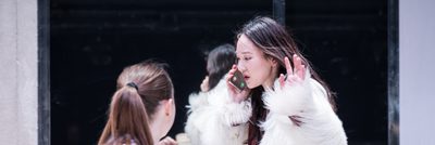 A woman is talking on a mobile phone. Another woman offers her a cup of tea but is ignored.